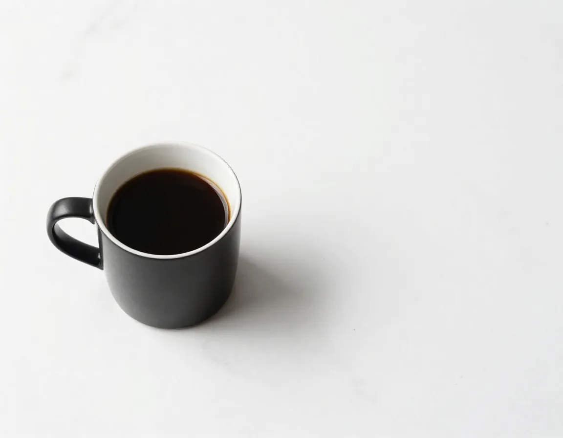 A minimalist black coffee mug on a white marble background with negative space